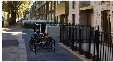 An image showing a row of houses with railing fences outside. Next to the pavement are several bicycles locked to bicycle racks. 