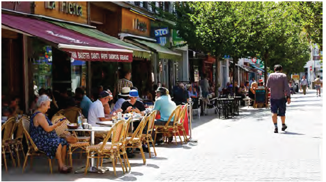 An image of a pedestrianised zone with cafes and businesses on the side of the road. The cafes have outdoor seating.